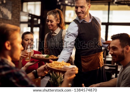 Happy waiters bringing food at the table and serving group of friends in a restaurant.
