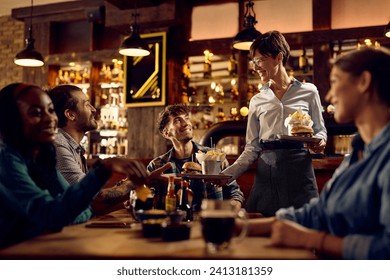 Happy waitress serving hamburger with French fries to group of guests in a bar. - Powered by Shutterstock