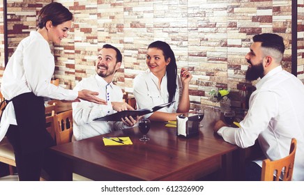Happy waitress taking order at table of people having dinner together