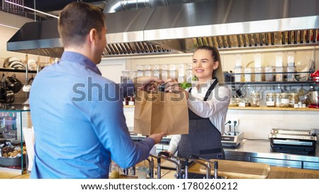 Happy waitress wearing apron serving customer at counter in small family eatery restaurant - Small business and entrepreneur concept with woman owner in eatery with takeaway service delivery