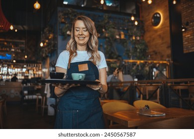 Happy waitress working at a restaurant and looking at the camera smiling. I Love My Job! Waitress is laughing and enjoying being at work, while she is holding coffee to be served to guests. - Powered by Shutterstock