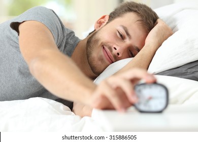 Happy wake up of a happy man lying on the bed and stopping alarm clock
