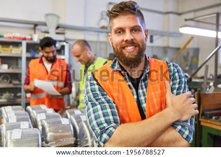 Happy warehouse worker in training in material warehouse of metal factory with colleagues