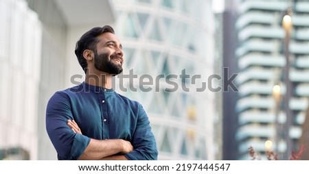 Happy wealthy rich successful indian business man standing in big city modern skyscrapers street on sunset thinking of successful future vision, dreaming of new investment opportunities concept.