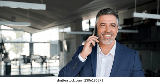 Happy wealthy successful mature business man talking on the phone in office. Smiling professional businessman executive entrepreneur wearing suit holding telephone making corporate call on cellphone. - Powered by Shutterstock