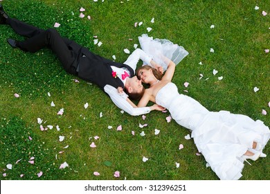 Happy wedding couple lying on green grass at the summer time