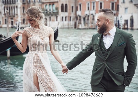 Happy wedding couple near the canal in Venice. Elegant woman in luxury ivory dress, messy updo hair, man in green three-piece suit and bow tie