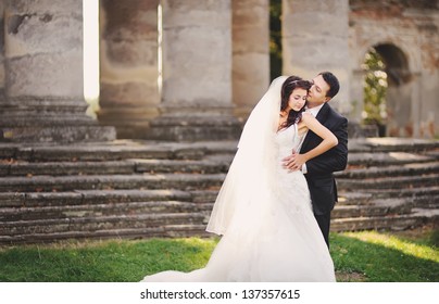 happy wedding couple next to columns of an old church embracing