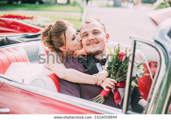 happy\
wedding portrait: a young wedding couple the bride and groom are\
sitting in their red wedding car and smiling\

