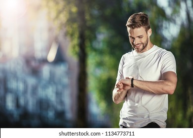 Happy well shaped male standing and looking at smartwatch during training. He is satisfied with results. Copy space in left side - Powered by Shutterstock