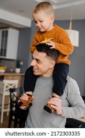 Happy White Father Smiling And Giving Shoulder Ride To His Little Son At Home