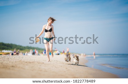Happy white woman running and playing on a beach with two welsh corgi pembroke dogs