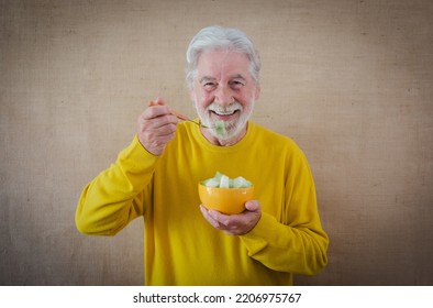 Happy White-haired Senior Man In Yellow Shirt Isolated On A Light Background Is Holding A Bowl With Cut Melon Ready To Be Eaten