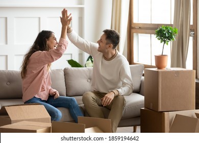 Happy wife and husband sit on couch near heap of belongings in boxes, giving high five congratulate each other with relocation, housing improvement, life changes, new first own house purchase concept - Powered by Shutterstock