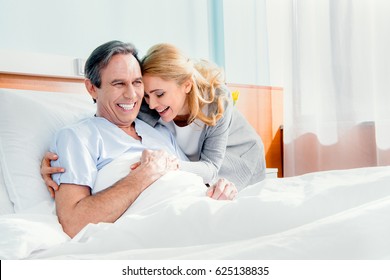 Happy Wife Visiting Smiling Elderly Husband In Hospital