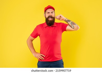 Happy winking man in casual red cap and tshirt twirling moustache yellow background, handyman