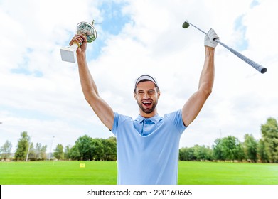 Happy winner. Happy male golfer holding trophy and driver while standing on golf course 