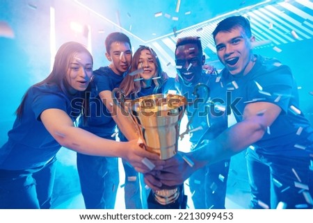 Happy Winner team gamer holding cup trophy prize of victors video games tournament. Concept cyber gaming esport. Soft focus, neon color.