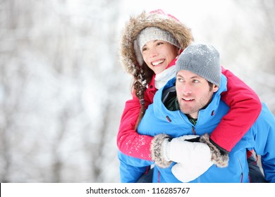 Happy winter travel couple. Man giving woman piggyback ride on winter vacation in snowy forest. Young interracial couple, Asian woman, Caucasian man. - Powered by Shutterstock