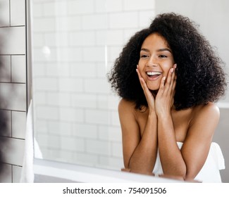 Happy woman admiring her skin in front of the bathroom mirror, touching face with hands - Powered by Shutterstock