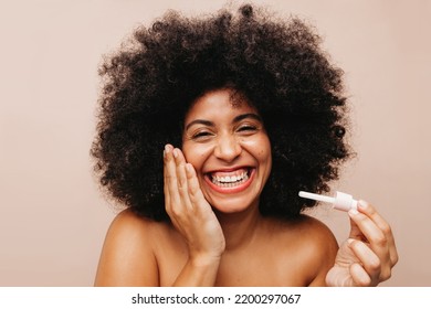 Happy Woman With Afro Hair Laughing Cheerfully While Applying Cosmetic Serum On Her Face. Gorgeous Young Woman Of Color Treating Her Skin With A Nourishing Beauty Product.