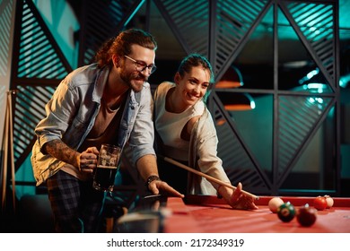 Happy woman aiming at the ball while playing snooker with her boyfriend in a pub. 