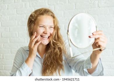 Happy woman applying cream and looking at mirror over grey background. Concept about body positivity, self esteem, and body acceptance