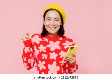 Happy woman of Asian ethnicity 20s wear red knitted sweater beret hold in hand use mobile cell phone do winner gesture isolated on plain pastel pink background studio. People lifestyle fashion concept - Powered by Shutterstock