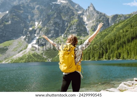 Happy woman with backpack near lake on wooded mountains background.  Hiking. Nature. Travel and tourism.