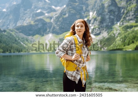 Happy woman with backpack near lake on wooded mountains background.  Hiking. Nature. Travel and tourism.