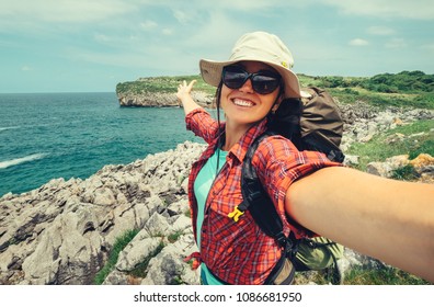 Happy woman backpacker traveler take a selfie photo on amazing ocean coast