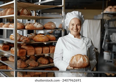 Happy woman baker chef holding bread standing near showcases - Powered by Shutterstock