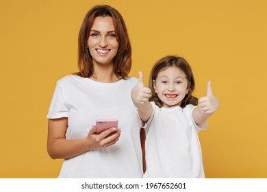 Happy Woman In Basic White T-shirt Have Fun Child Baby Girl 5-6 Years Old Hold Use Mobile Cell Phone Mom Little Kid Daughter Isolated On Yellow Color Background Studio Mother's Day Love Family Concept