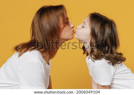Happy woman in basic white t-shirt have fun kiss with cute child baby girl 5-6 years old. Mommy little kid daughter isolated on yellow orange color background studio. Mother's Day love family concept