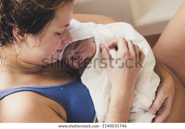 Happy woman in bath holds her amazing newborn\
baby in hands after natural water birth. During childbirth, giving\
birth. Vintage film grain\
effect.