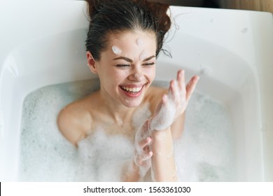 Fröhliche Frau badet in einer Badewanne mit weißem Schaumstoff auf ihrem Gesicht Spaß Emotionen