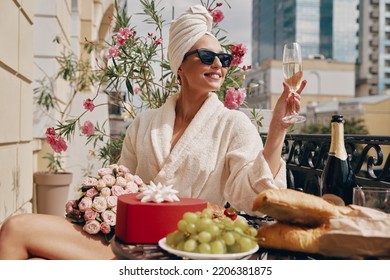 Happy woman in bathrobe enjoying champagne while having brunch on the balcony - Shutterstock ID 2206381875