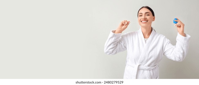 Happy woman in bathrobe using dental floss on light background with space for text