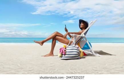 Happy woman at the beach on beach deck chair, sunbathing, uses mobile phone, in a sunny day with blue sky, concept a summer beach holiday, online shopping, booking travel, and resorts accommodations - Powered by Shutterstock