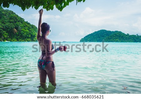Happy woman in bikini relaxing on sea beach her hand holding cup of coffee, Andaman sea, Mu Koh Surin national park, Phangnga, Thailand