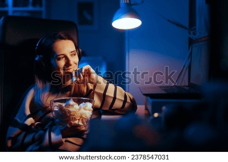 
Happy Woman Binging a Show Eating Potatoes Chips at Night. Cheerful girl watching a movie having a late snack in front of a screen
