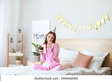 Happy Woman With Birthday Cake And Party Whistle In Bedroom At Home