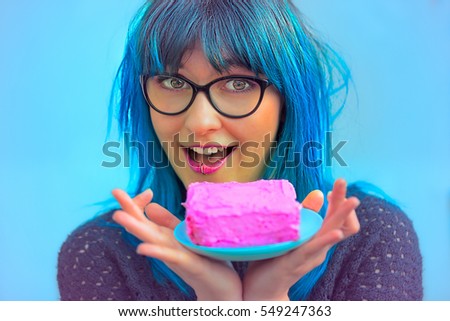 A happy woman with blue hair and pink cake on a plate in her hands