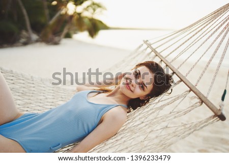 Happy woman in blue swimsuit is lying on a hammock on the nature and looking at the camera                             