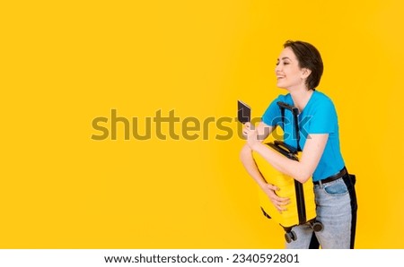 happy woman in blue t-shirt with yellow suitcase and passport on yellow background. Copy space. Travel enjoy concept