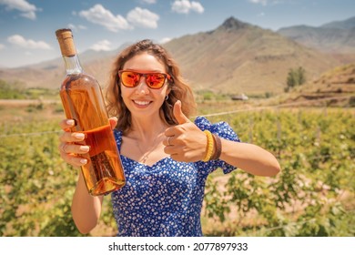 Happy woman with a bottle of grappa or cognac on the background of a vineyard. Strong alcohol spirits from the richest grape varieties