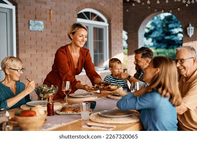 Happy woman bringing food at dining table while having meal with her extended family on a patio. - Powered by Shutterstock