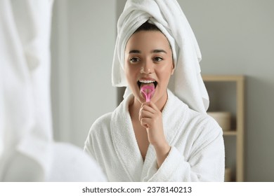 Happy woman brushing her tongue with cleaner near mirror in bathroom