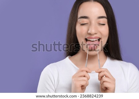Happy woman brushing her tongue with cleaner on violet background, space for text
