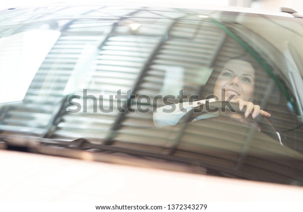 Happy woman buyer examines her new vehicle in\
car dealership